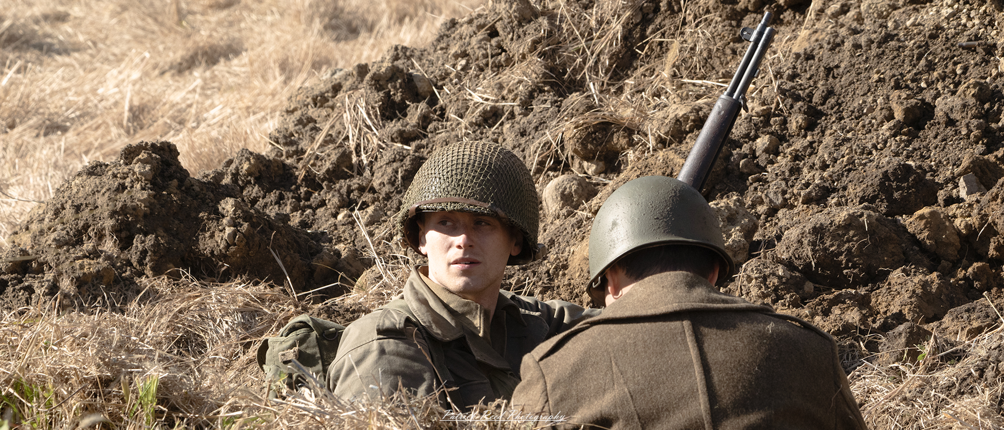 "U.S. GI soldier in a foxhole during World War II, embodying the spirit of resilience and vigilance in combat. The soldier is crouched inside the makeshift shelter, surrounded by dirt and sandbags, with a rifle at the ready. His expression reflects focus and determination as he scans the environment for potential threats. The foxhole is set in a war-torn landscape, emphasizing the harsh realities faced by soldiers. This image highlights the bravery and strategic mindset of American troops during the conflict."
